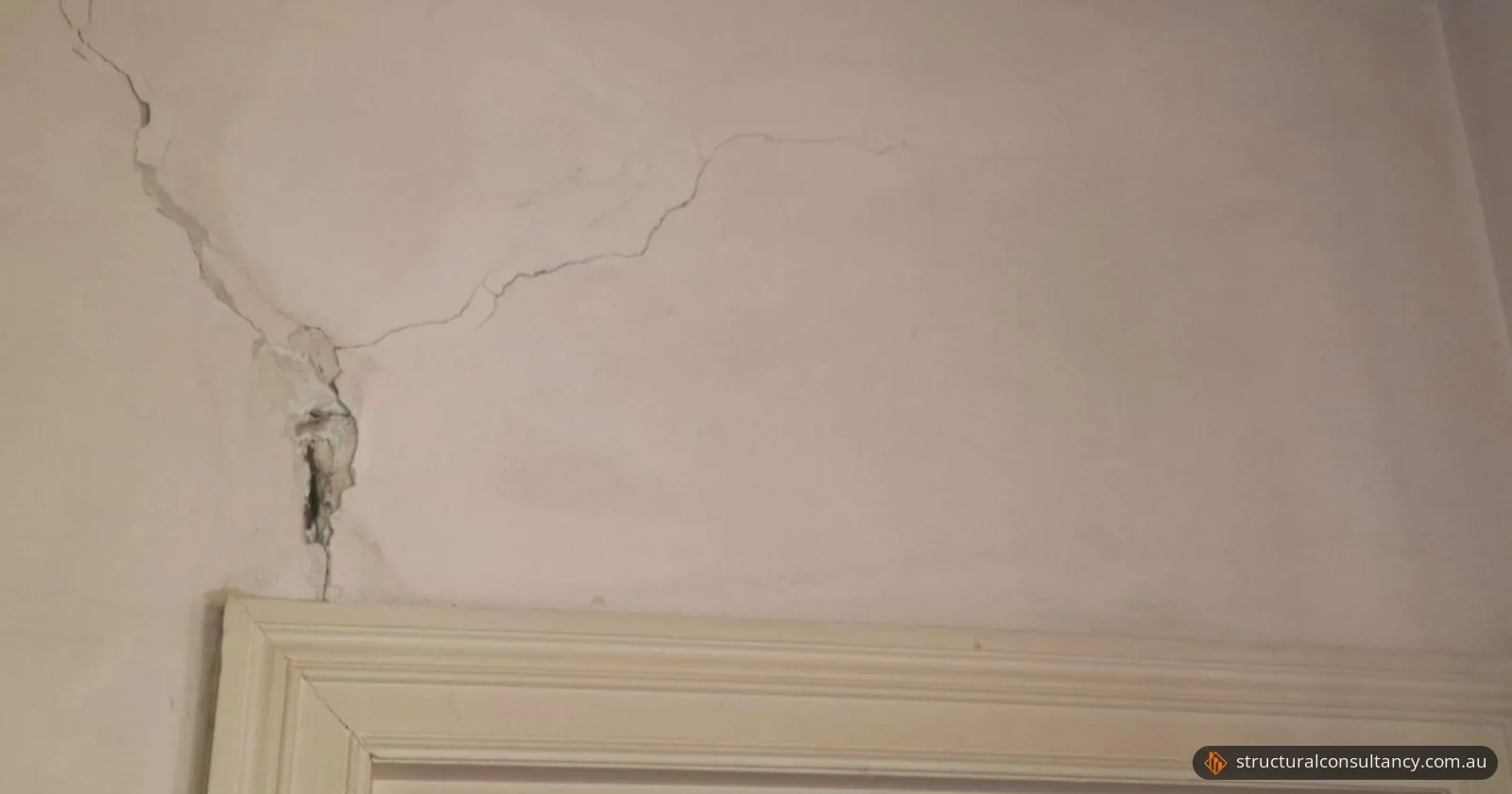 Branching crack and lost plaster in a wall above a timber doorway